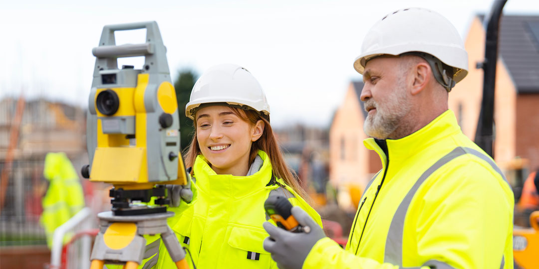 Surveying team in bright safety jackets conducts land measurements on construction site